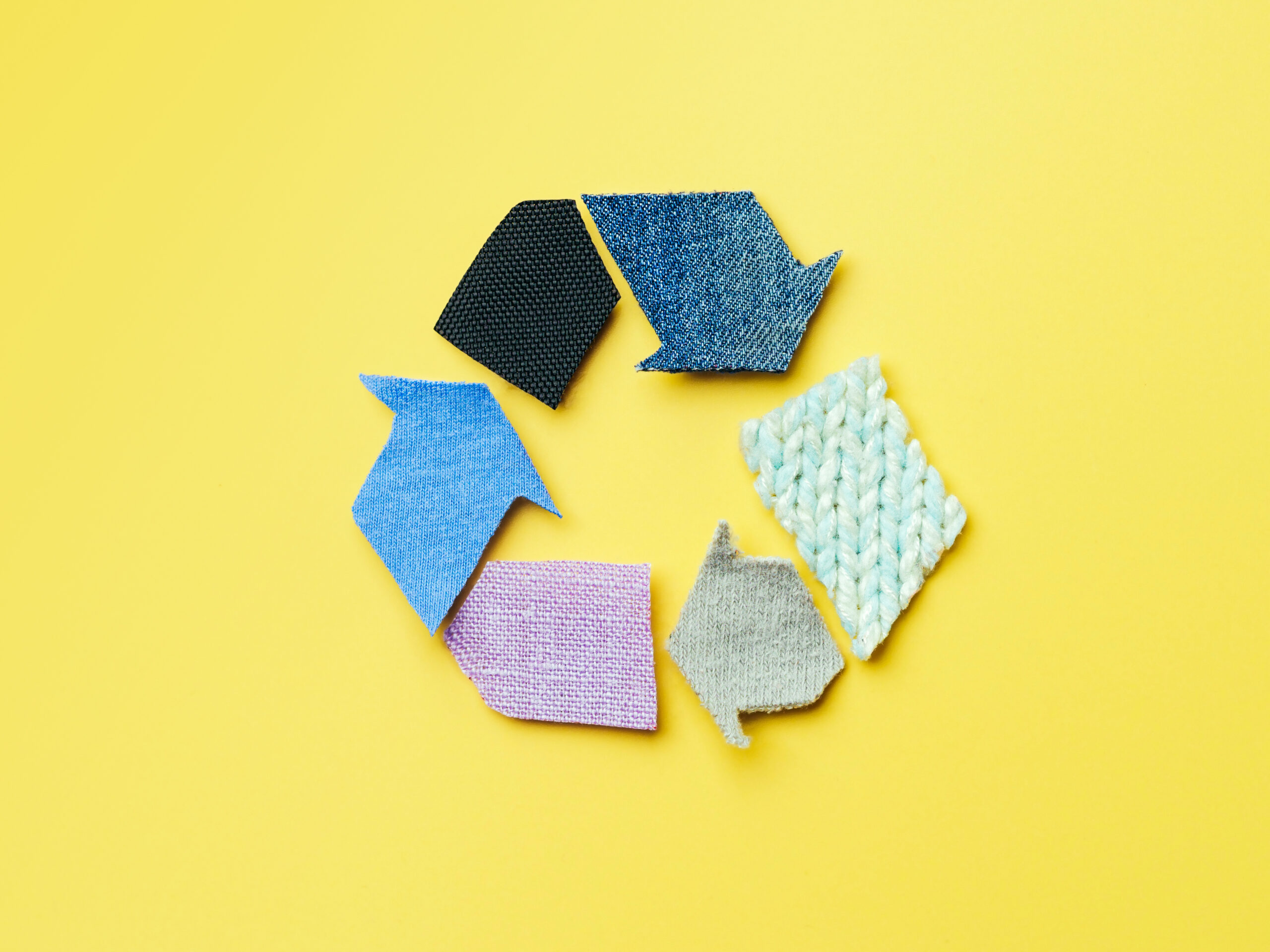 Hintergrund zum Konzept „Wiederverwenden, Reduzieren, Recyceln“. Recycling-Symbol aus alter Kleidung auf gelbem Hintergrund. Draufsicht oder Flatlay.