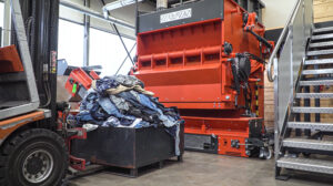 Eine Kisten voller Jeans vor einem orangenen WEIMA Shredder