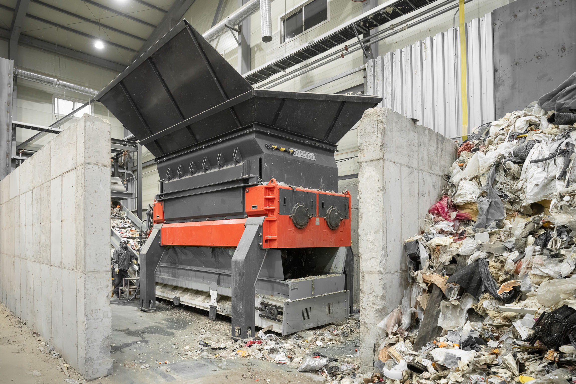 An orange shredder with a large hopper next to a pile of trash.