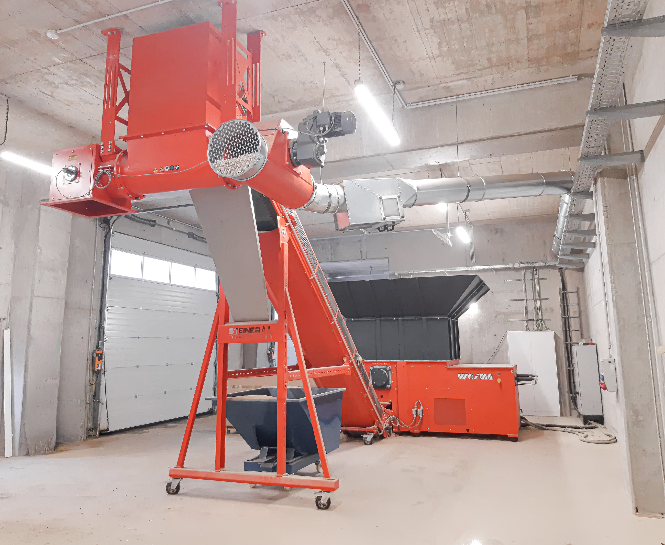 An orange shredder in a warehouse with an attached screw conveyor.