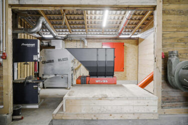 an orange single-shaft shredder sits in front of wood waste in a woodworking shop