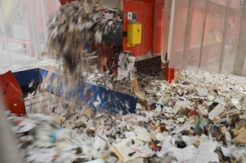 Geshredderte Zeitungen fallen aus der Maschine auf das Förderband.