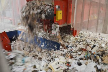 Shredded newspapers fall from the machine onto the conveyor belt.