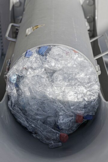 Ein Pressling aus Plastikflaschen wird gerade aus dem Auswurf des Entwässerers geschoben
