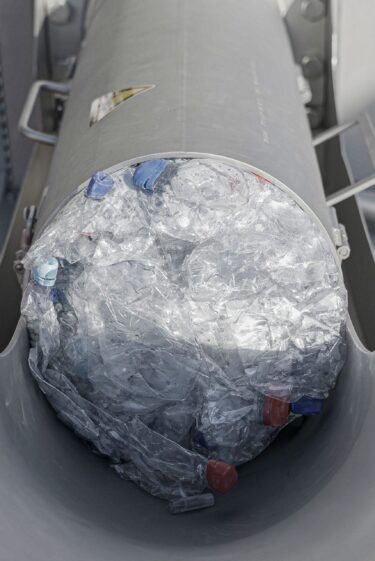 Ein Pressling aus Plastikflaschen wird gerade aus dem Auswurf des Entwässerers geschoben
