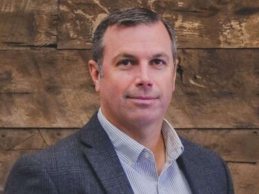 Mr. Madison Burt stands before a wooden accent wall wearing a sport coat and collared shirt