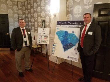 Jeremy Boggs and Madison Burt pose in front of a map of SC recycling companies and sponsors of the event