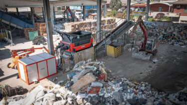 orange weima shredder with hydraulic drive and piles of household waste