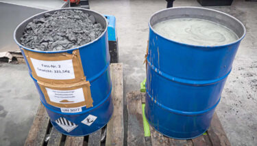 two blue barrels with separated dry grinding sludge and coolant after draining and compressing