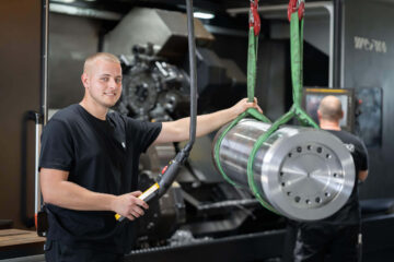 WEIMA Mitarbeiter steht vor einem CNC-Fräszentrum, rechts daneben ein Rohling eines WEIMA Rotors