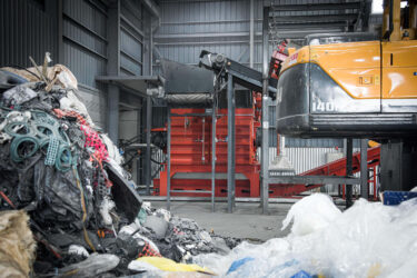 Ein orangener Shredder in Südkorea der alte Textilien zerkleinert die im Vordergrund liegen.