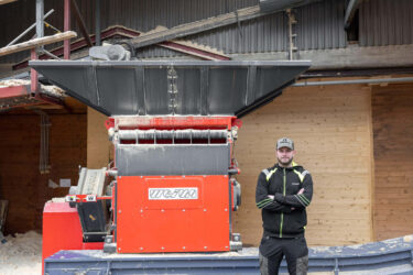 Eine rote WEIMA S7.15 steht vor einem Gebäude. Daneben steht ein Mitarbeiter der Firma und schaut in die Kamera.