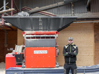 A red WEIMA S7.15 is standing in front of a building. A company employee stands next to it and looks into the camera.
