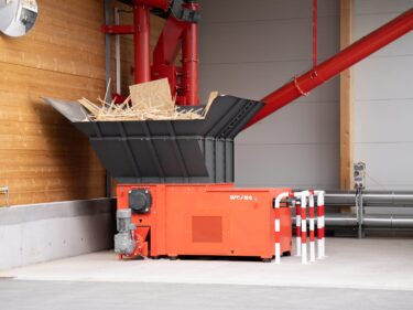 The WLK 1500 single-shaft shredder from WEIMA stands in front of a building. In the background is the associated control cabinet and the transport system consisting of screw conveyors and spirals.