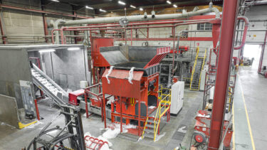 View from above into an industrial hall, in the centre is an orange-red shredder, in the foreground you can see a forklift truck