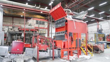 Orange-roter Shredder von WEIMA in Bildmitte, links daneben ein Austragsförderband, in einer industriellen Halle umgeben von Recycling-Anlagentechnik