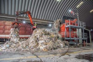 Abfallberg links, orangener WEIMA Schredder rechts in einer Lagerhalle