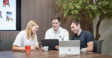 zwei Männer und eine Frau sitzen gemeinsam als Team an einem Tisch vor Laptops