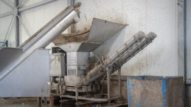 Eine silberne Entwässerungspresse aus Edelstahl bei der Entwässerung von Kunststoff Feinanteilen in einer Industriehalle