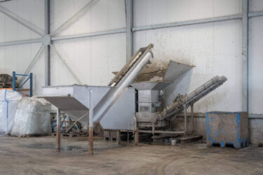 Eine silberne Entwässerungspresse aus Edelstahl bei der Entwässerung von Kunststoff Feinanteilen in einer Industriehalle