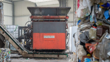 Ein orangefarbener Shredder in einer Industriehalle mit Post-Consumer Müll im Vordergrund