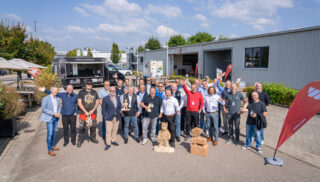 Eine Gruppe an lachenden Männern vor einem Firmengebäude.