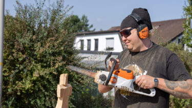Ein Mann schnitzt mit einer Motorsäge eine Figur aus einem Holzblock