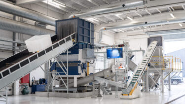 Several IBC containers are transported into the WEIMA shredder, in the background of the hall a granulator and a friction washing system