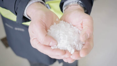 ein Mensch in einer schwarz gelben Jacke hält IBC Rezyklat nach dem Recyclingprozess in der Hand