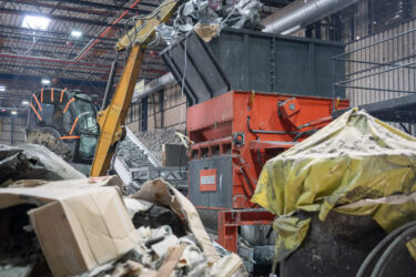 Ein WEIMA Zerkleinerer wird mit Hilfe eines Baggers beladen, im Vordergrund sieht man einen Haufen Industrieabfälle