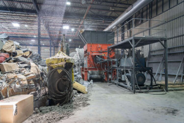 Ein WEIMA Shredder steht in einer Industriehalle, davor der Hydraulikantrieb und Industriemüll