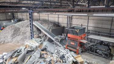 Ansicht von oben auf einen WEIMA Shredder mit Förderband. Material zur Zerkleinerung liegt im Bereich vor dem Shredder, nach dem Förderband kommt das zerkleinerte Material