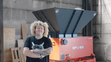 A man with blond hair in front of an orange shredder