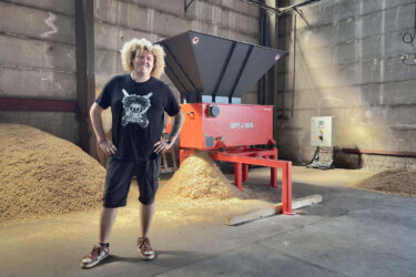Ein Mann mit blonden Haaren vor einem orangefarbenen Shredder