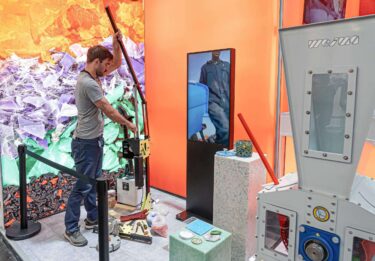 Precious Plastic mit Shredder Pro auf der K 2022 Messe, Mitarbeiter bedient eine Spritzgussmaschine
