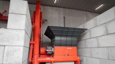 An orange shredder in the middle of large concrete blocks with screw conveyor