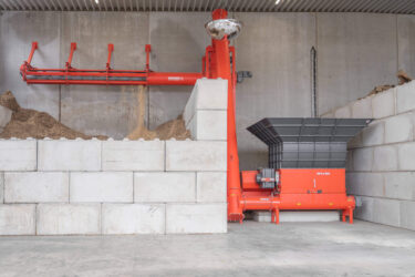 In einer überdachten Halle steht ein WEIMA Zerkleinerer mit Förderschnecke, die das zerkleinerte Material in einen Bunker befördert.