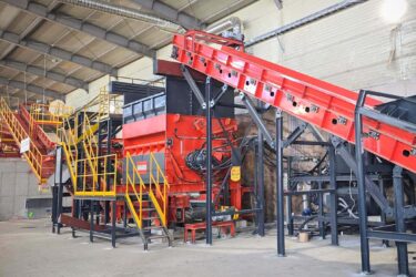 An orange shredder in a warehouse built into a recycling line with conveyor belts