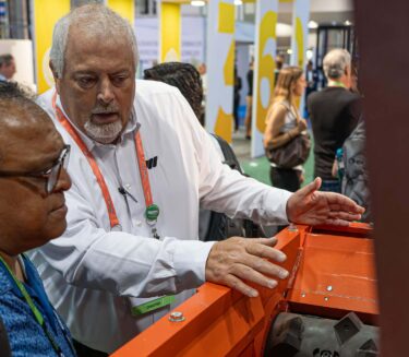 A salesman wearing white stands next to a man wearing a blue shirt and an orange machine.