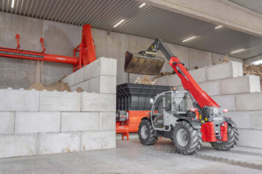 A telescopic loader transports wood scraps into a large hopper for further processing.