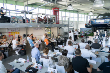 Ein Mann hält einen Vortrag über Restholzmanagement, er steht in Mitten von alten Oldtimer der WEIMA Garage