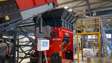 An orange shredder in a warehouse with a conveyor belt and a roll feeder with BOPP film.
