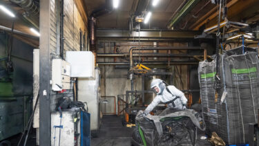 Ein Mann in einem weißen Schutzanzug mit einem leeren schwarzen Big Bag in der Hand in der Halle eines Reifenherstellers.
