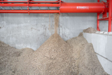 A red screw conveyor transports wood chips.