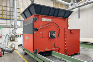 Orange shredder with green conveyor belt in a warehouse