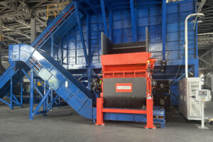An orange shredder with a blue conveyor belt in a warehouse