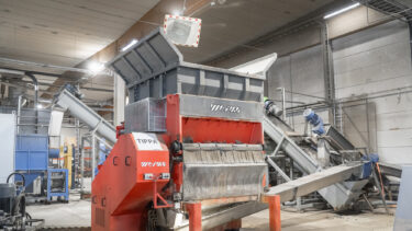 An orange shredder in a warehouse with an attached screw conveyor