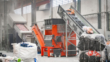 The WEIMA machine in a hall, with a conveyor belt and industrial plastic waste in front of it