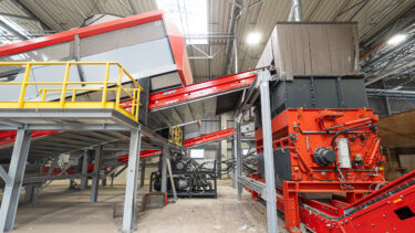 Ein orangener WEIMA PowerLine shredder, verbunden mit einem großen Förderband