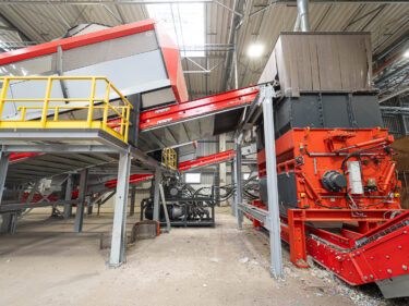 Ein orangener WEIMA PowerLine shredder, verbunden mit einem großen Förderband